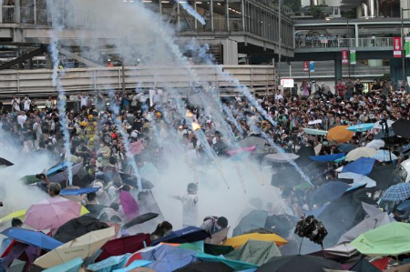 Protesters with umbrellas open as tear gas cannisters fly at them.